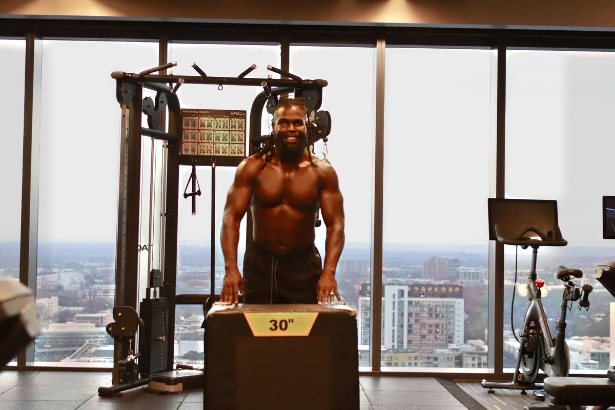 Mario Bonds shirtless in a high-rise skyline gym, a lean muscular physique, ready to train.