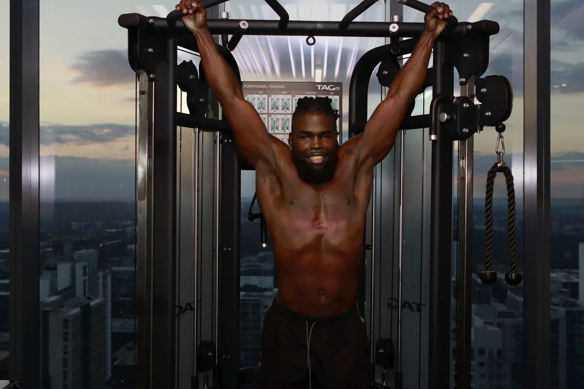 Mario Bonds training shirtless in a sunlit high-rise gym, the city skyline through floor-to-ceiling windows.